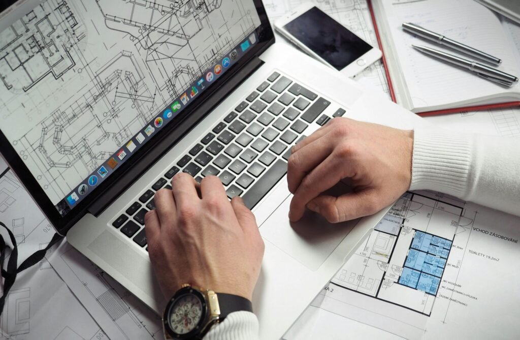 Architect reviewing detailed floor plans and schematics on a laptop with a smartphone nearby.